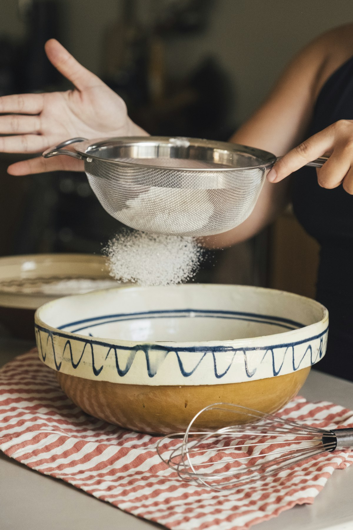 Sifting flour into a ceramic bowl with a whisk