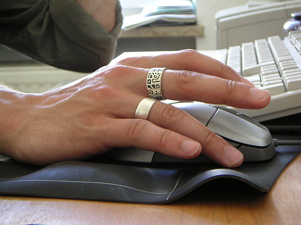 Male hand with two rings operating computer mouse