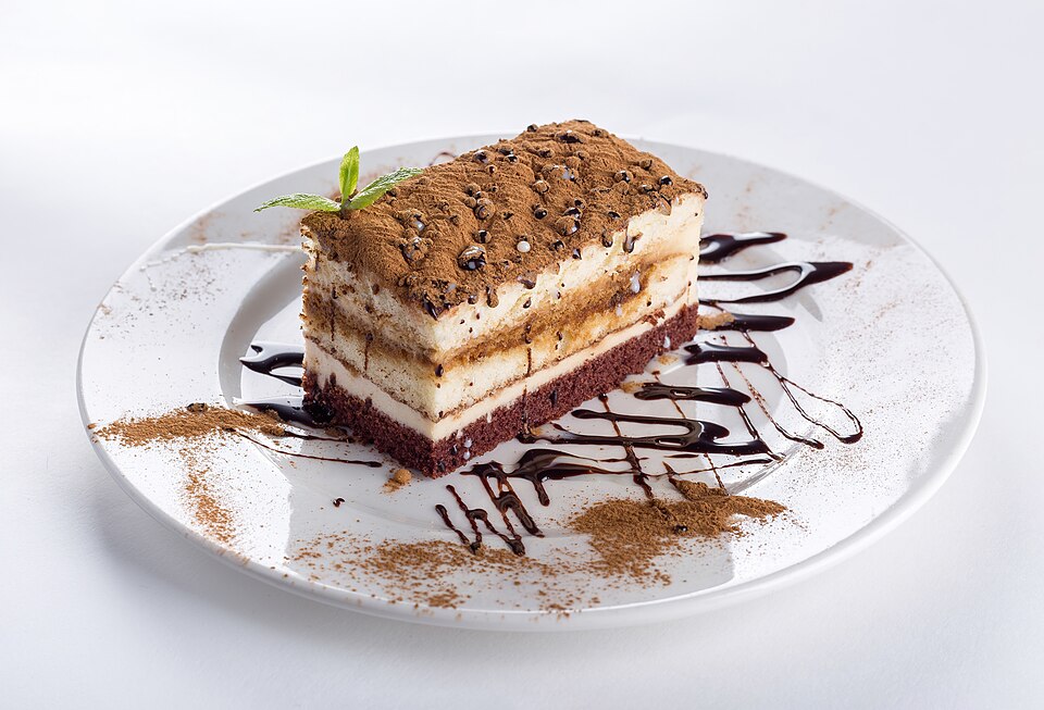 Piece of chocolate cake on a white plate decorated with chocolate sauce