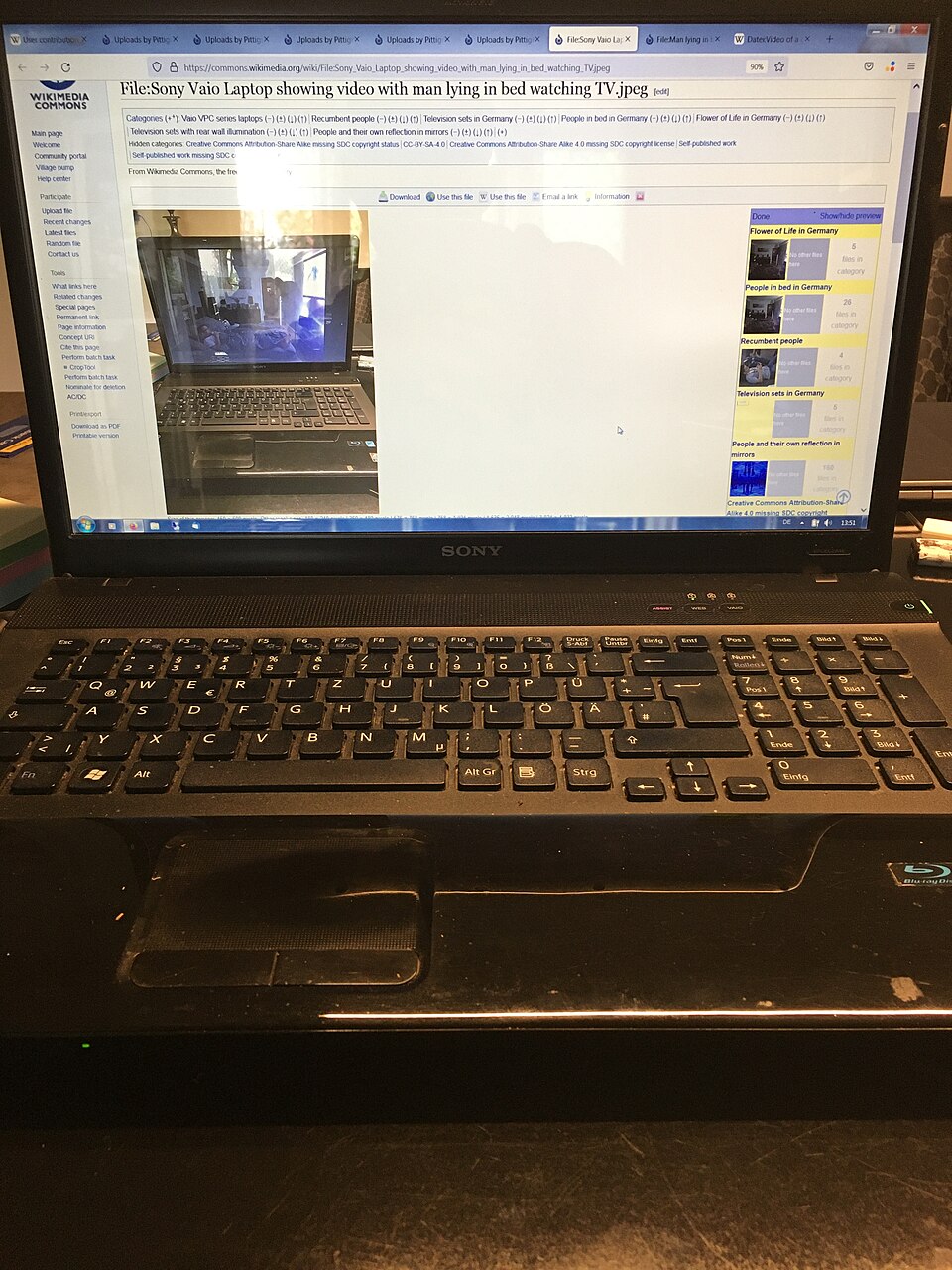 Image with nested realities of a laptop showing a Wikimedia Commons file with the same laptop showing video of man watching TV