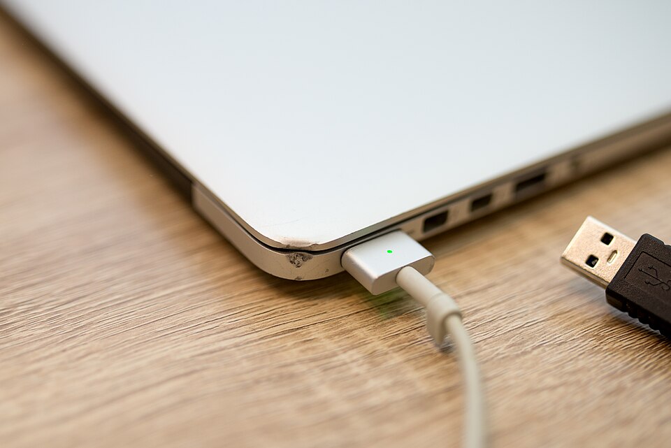 Charging a laptop with a USB cable on a wooden table in a cozy environment during daytime