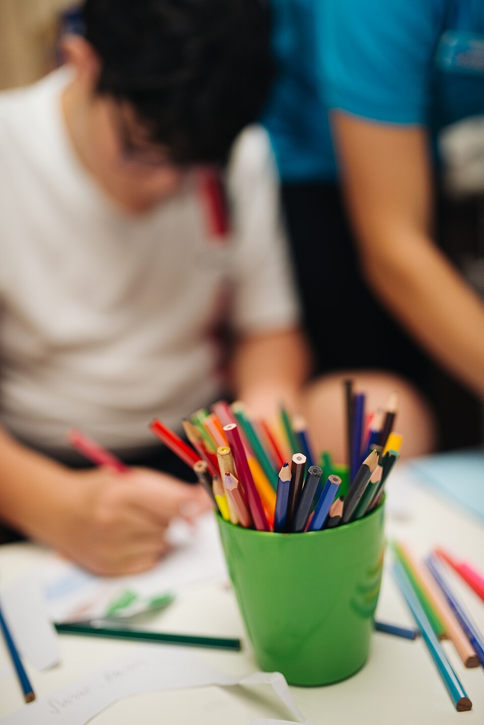 Young children sit at a table, using colored pencils to create art