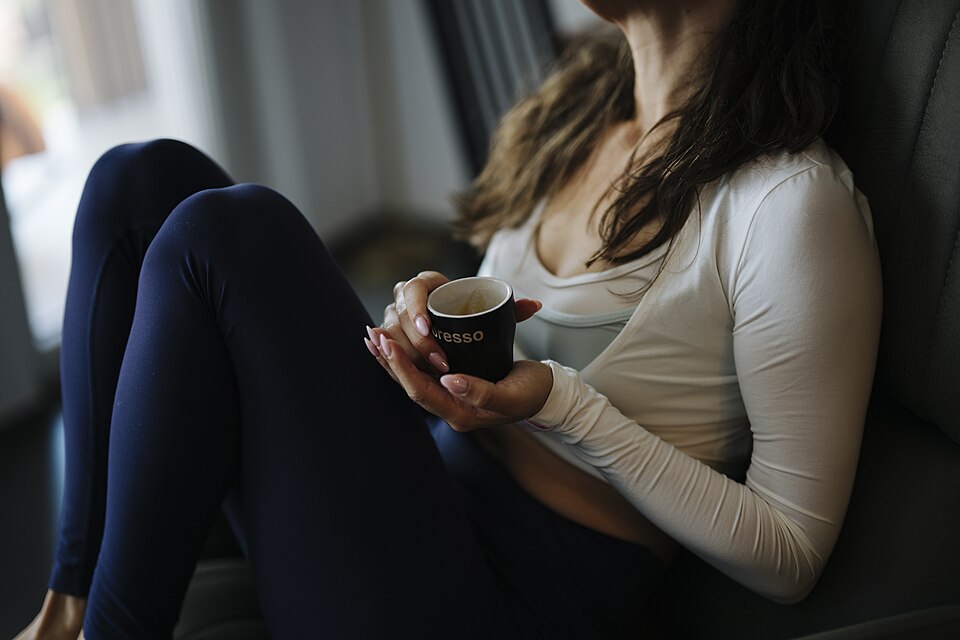 Woman sits on a chair holding a coffee cup in a cozy indoor setting