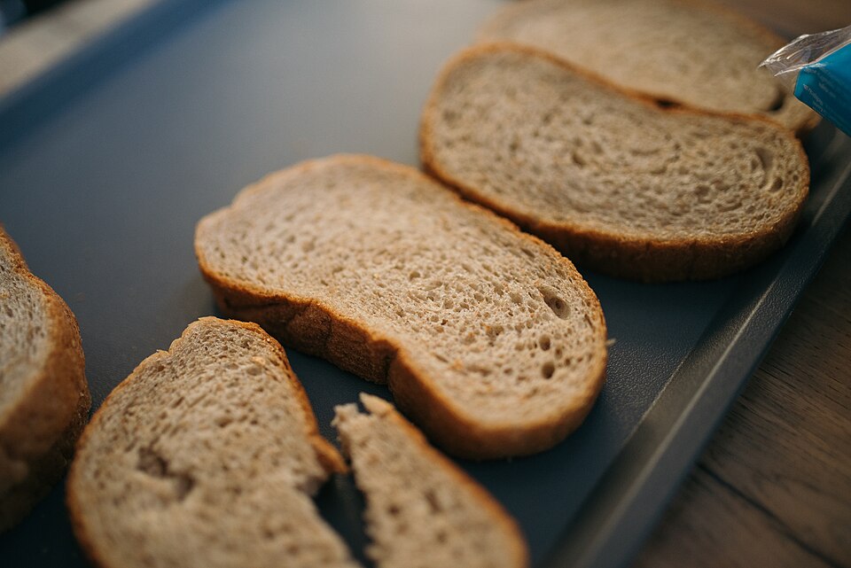 Fresh slices of bread arranged on a baking tray in a kitchen setting