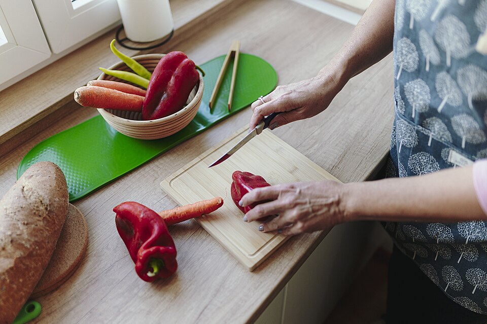 Woman prepares vegetables in kitchen with cutting board and knife during meal preparation